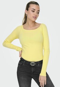 Geel geribbeld langsl sleeves top met een vierkante halslijn, gestyled met hoge zwarte jeans en een zwarte riem met een zilveren dubbele ringgesp.