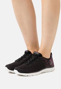 Zapatillas deportivas negras con una parte superior de malla texturizada, con acentos en rosa y suela de goma blanca. Diseño minimalista con cierre de cordones.