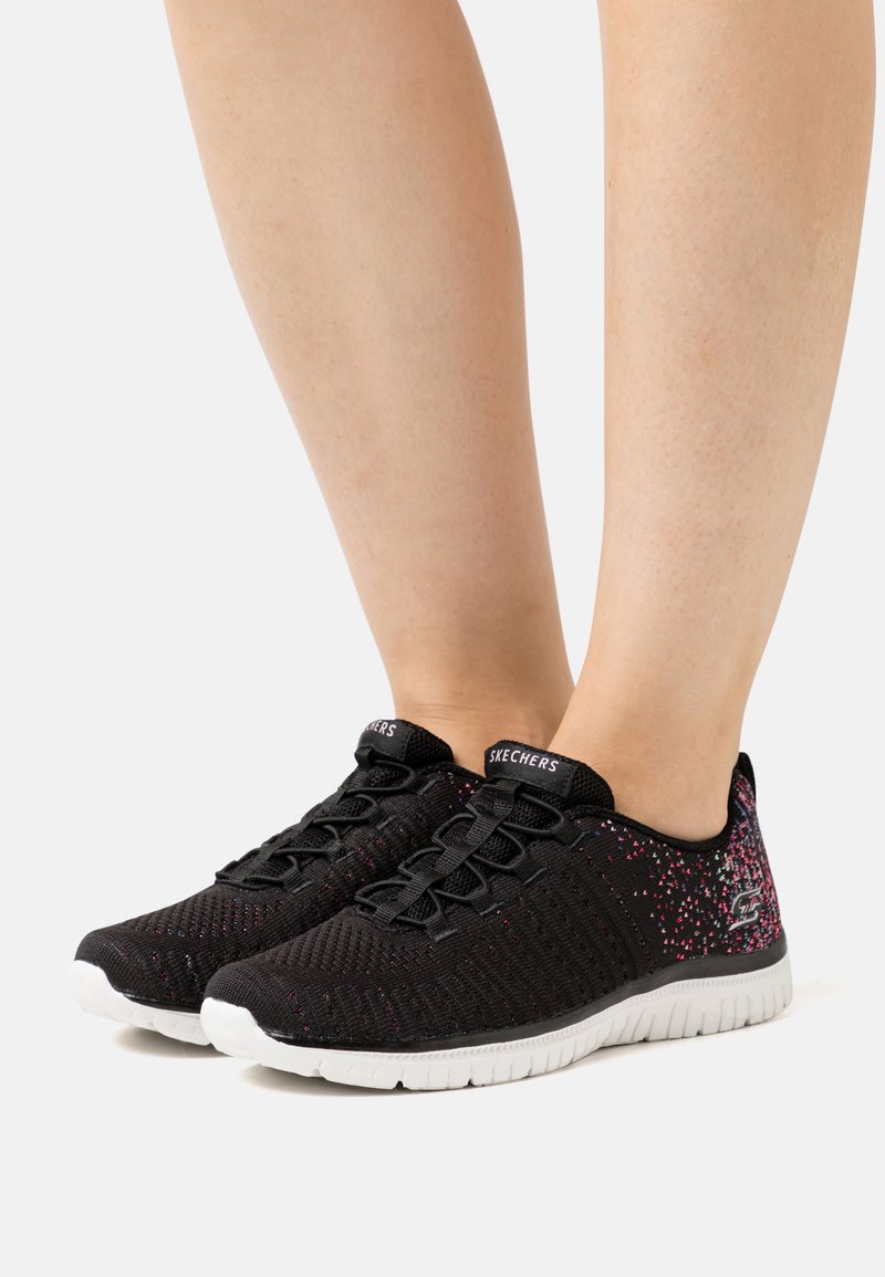 Zapatillas deportivas negras con una parte superior de malla texturizada, con acentos en rosa y suela de goma blanca. Diseño minimalista con cierre de cordones.