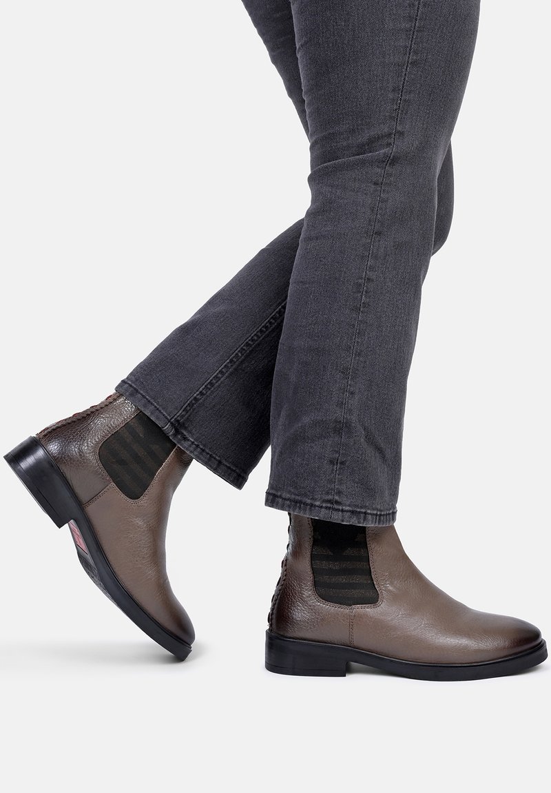 Brune læder Chelsea støvler med elastiske sidepaneler og tekstureret overflade. Sorte gummisåler med subtil branding, parret med mørkegrå jeans.