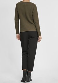 Pull texturé vert olive avec un col rond, associé à un pantalon noir droit et des bottes à talons noires. Design simple et contemporain.