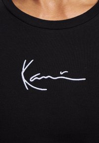 T-shirt in cotone nero con firma ricamata bianca. Design a girocollo con texture morbida, vestibilità aderente e stile minimalista.