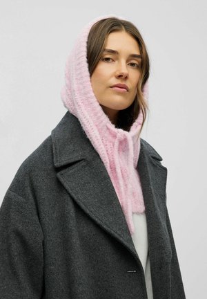 Capucha de punto rosa con un acabado suave y texturizado, llevada debajo de un abrigo de lana gris oscuro con solapas muestradas y cuello abierto.