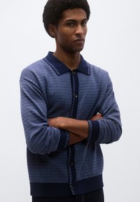 Ναυτικό μπλε πλεκτή ζακέτα με υφή με σχέδιο, γιακά, κουμπώματα και αντίθετες λεπτομέρειες στα μανίκια και το τελείωμα.