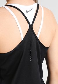 Sort atletisk tanktop med racerback-design og hvide stropper. Det har et tekstureret stof og seks små cirkulære detaljer på ryggen.