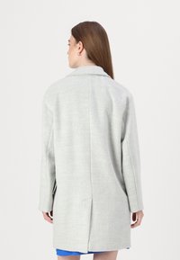 Cappotto grigio chiaro in misto lana con collo a falde, maniche lunghe e tasche laterali. Presenta una linea dritta e uno spacco posteriore per facilitare i movimenti.