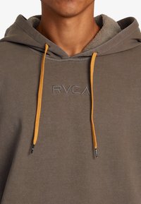Grijze hoodie met oranje trekkoorden, voorzien van een zachte binnenvoering en geborduurd RVCA-logo. Normale pasvorm en textuurstof.