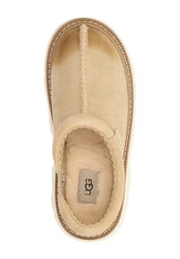 Tan suede instapper met een zachte bontvoering, voorzien van een ronde neus en contrasterende stiksels langs de randen. Logo label zichtbaar aan de binnenkant.