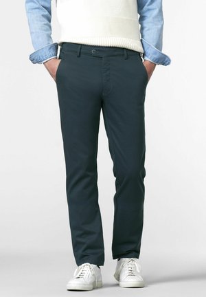 Chinos vert foncé en coton lisse, présentant une coupe slim, des poches latérales et une fermeture à bouton, assortis à des baskets blanches et un haut clair.