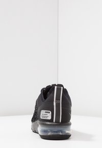 Czarny but sportowy z teksturowaną cholewką, półprzezroczystą podeszwą z poduszką powietrzną, odblaskowymi akcentami i metką na pięcie.