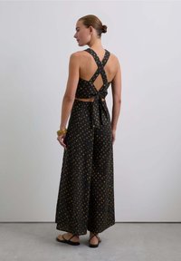 Conjunto de dos piezas negro con un top de espalda cruzada y pantalones de pierna ancha, con patrones geométricos coloridos y un detalle de cintura anudada.