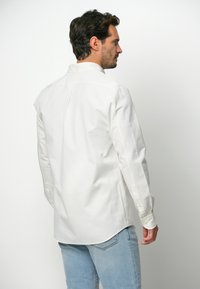 Witte lange mouwen shirt met knoopmanchetten, klassieke kraag en rugplooi-detail, gecombineerd met lichtblauwe jeans. Soepele stoftextuur.