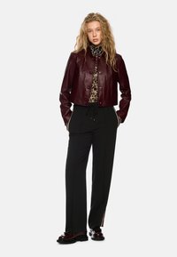 Burgundy cropped leather jacket with snap buttons, paired with black high-waisted pants featuring side stripes. Notable leopard print top underneath.