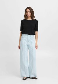 Sort ribbet kortærmet top, parret med lys blå højhævede bredde ben jeans. Bemærkelsesværdige sømme og struktureret stof. Brune flade sko.