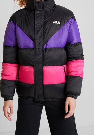 Person trägt eine schwarze Steppjacke mit lila und pinken Farbfeldern, vordere Druckknöpfe und FILA-Logo auf der Brust, kombiniert mit schwarzen Hosen.