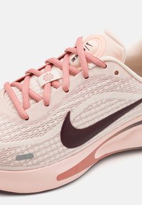 Nike løpesko med et lett rosa nettingoverside, mørk rosa detaljer, flate lisser og en tykk, polstret såle med lagdelte detaljer.