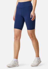 Shorts da ciclismo a vita alta di colore blu navy, realizzati in tessuto elasticizzato, con un design senza cuciture e orlo arrotondato, abbinati a scarpe sportive bianche.