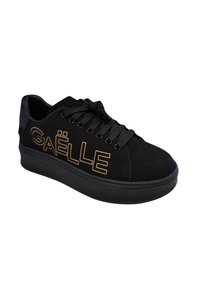 Sneaker in suede nero con suola spessa nera, caratterizzata da vistosa scritta dorata "GAËLLE", chiusura con lacci e dettagli testurizzati sulla parte superiore.