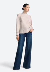 Bluzka w paski w jasnoróżowym i białym kolorze, z wysokim dekoltem ozdobionym falbanką, zestawiona z ciemnoniebieskimi dzwonowatymi jeansami, prezentującymi luźny krój.