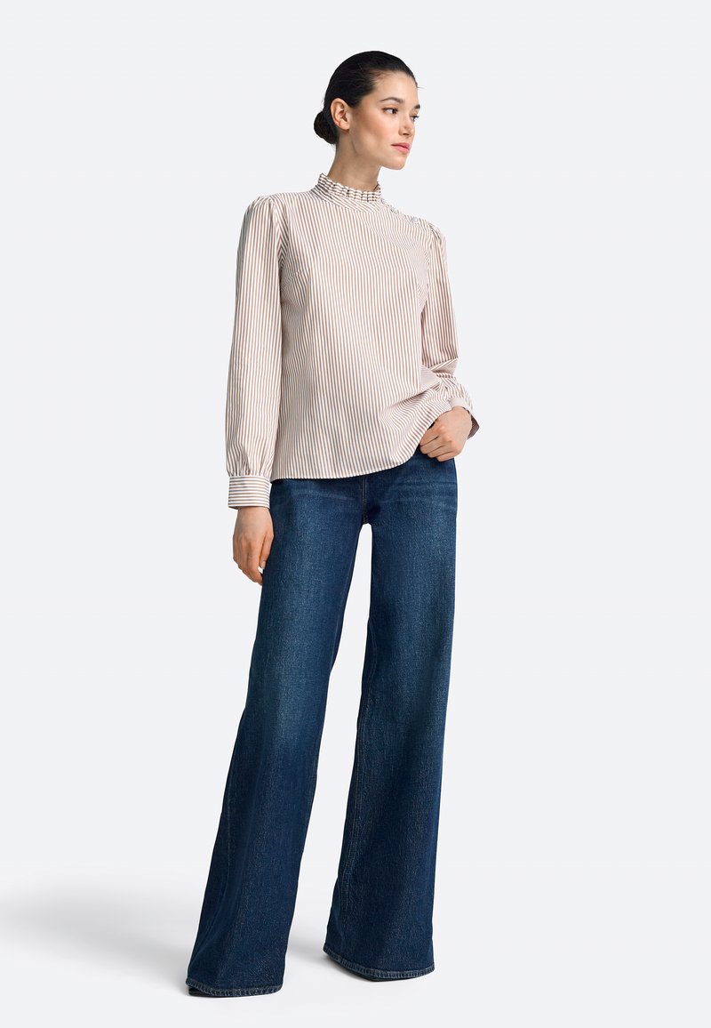 Bluzka w paski w jasnoróżowym i białym kolorze, z wysokim dekoltem ozdobionym falbanką, zestawiona z ciemnoniebieskimi dzwonowatymi jeansami, prezentującymi luźny krój.