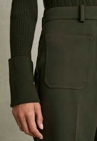 Top lung cu manșon lung, de culoare verde închis, cu dungi, asortat cu pantaloni cu talie înaltă, care au o curea plată pe spate, textură netedă și croială ajustată.