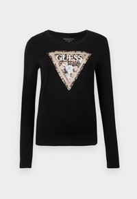 Črna majica z dolgimi rokavi iz mehke tkanine, z velikim trikotnim motivom z metalnim robom in stiliziranim napisom "GUESS".