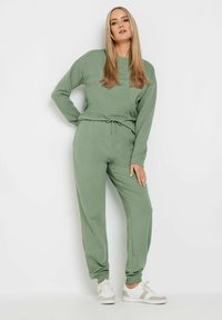 Felpa verde in cotone a maniche lunghe, abbinata a pantaloni jogger coordinati con una cintura regolabile. Sneakers bianche.