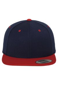 Sötétkék snapback sapka piros karimával. Texturált anyagból készült, piros szellőzőnyílásokkal és kör alakú címkével a karima szélén.