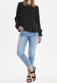 Schwarze Bluse mit weißen Punkten, mit gerafftem Bund und puffigen Ärmeln. Kombiniert mit hellblauen Skinny Jeans und schwarzen Sandalen mit Riemen.