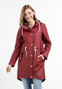 Cappotto impermeabile rosso con cappuccio, cordoncini bianchi, bottoni a pressione e due tasche frontali. Texture liscia con un taglio di lunghezza media.