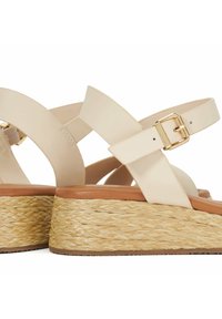 Beige wedge sandalen met een gevlochten jute zool, voorzien van soepele banden, een gespsluiting en een ronde teenontwerp.