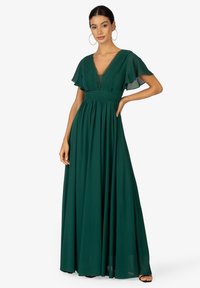 Lungo vestito verde smeraldo realizzato in tessuto leggero, caratterizzato da maniche a svolazzo, scollo a V profondo e vita arricciata, con dettagli di pieghe sottili.