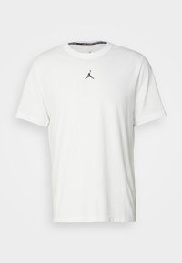 Vit bomull t-shirt med korta ärmar, med en svart Jumpman-logotyp på bröstet och svart krage. Slät textur.