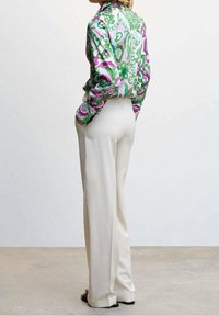 Blouse à manches longues, multicolore avec des motifs floraux verts, roses et blancs, associée à un pantalon large taille haute de couleur crème.