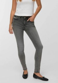 Jeans de mezclilla gris de corte slim con un ligero desgaste, cinco bolsillos, y bailarinas negras con un detalle de lazo, combinadas con una camiseta blanca sin mangas.