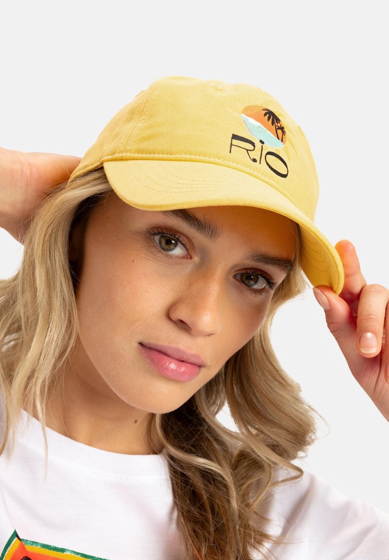 Yellow cotton baseball cap featuring a printed design of a sunset and palm trees, with the text "R.I.O." below the graphic.