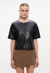 Top curto de pele preta com mangas curtas e decote redondo, apresentando uma textura suave e detalhes de costura. Combinado com uma saia xadrez.