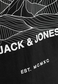 Juodas marškinėlis su balta linijine meno interpretacija abstrakčių kalnų, viršuje matyti ryškiai spausdintas prekės ženklas "JACK & JONES" ir užrašas "EST. MCMXC."