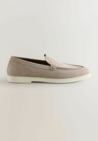 Mocassin beige en daim à enfiler avec une semelle en caoutchouc blanche, un bout arrondi et des coutures détaillées le long de la partie supérieure et des côtés.