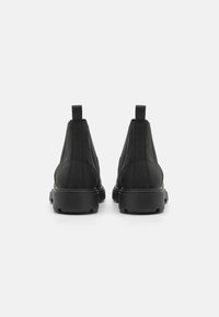 Bottines noires avec une tige en cuir lisse, des panneaux élastiques sur les côtés et une semelle en caoutchouc épaisse. Équipées d'une languette pour un enfilage facile.