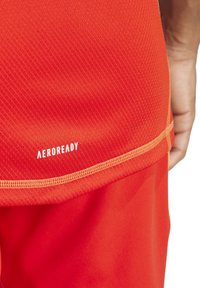 Rode sportieve shorts met een gestructureerd mesh-paneel en een AeroReady-logo aan de zoom, omlijnd met een contrasterende gele stiksel.