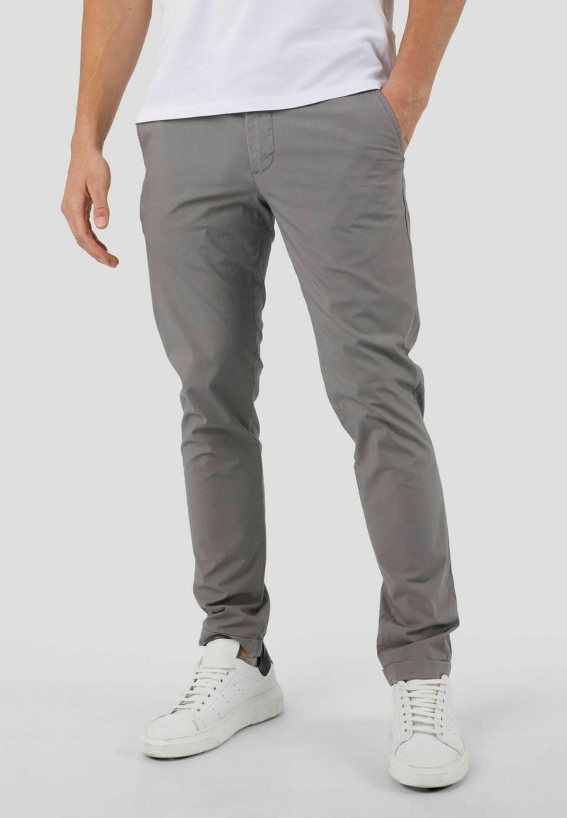 Chinos de mezcla de algodón grises con corte ajustado, con bolsillos delanteros y traseros y una textura suave, combinados con zapatillas blancas.