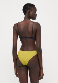 Fekete bikini felsőrész vékony pántokkal és kapcsos záródással, sárga, texturált, magas derekú bikini alsóval párosítva, melynek szegélye le van varrva.