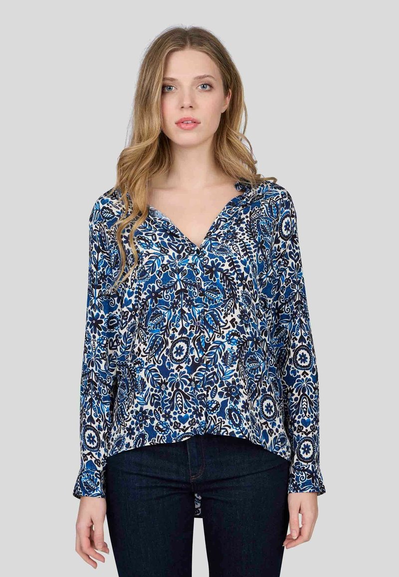 Blouse à manches longues avec un motif floral bleu, noir et blanc. Elle présente un décolleté en V et une coupe décontractée en tissu doux et léger.