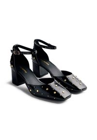 Chaussures à talons blocs en cuir verni noir avec bouts carrés, ornées d'accents en studs dorés et de brides ajustables à la cheville. Surface texturée brillante.