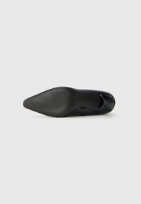Semelle de chaussure noire à bout pointu avec un avant à texture antidérapante et un talon lisse, présentée sur un fond clair et uni.
