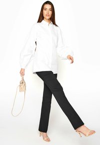 Vit blus med långa ärmar och ballongärmar, matchad med svarta, skräddarsydda byxor. Ljusbeige handväska och nakna högklackade sandaler.