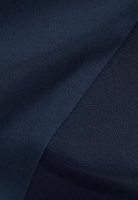 Tessuto blu scuro che presenta una texture liscia, con leggere variazioni nel tessuto che creano una profondità di colore e una leggera lucentezza.