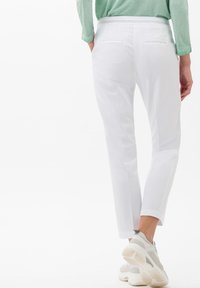Pantaloni bianchi alla caviglia con una texture liscia, abbinati a scarpe da ginnastica grigie e bianche. Il design sul retro presenta due tasche con cuciture sottili.