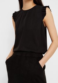 Svart ärmlös topp med volangdetaljer på axlarna, tillverkad av ett mjukt tyg, med avslappnad passform och rund halsringning.